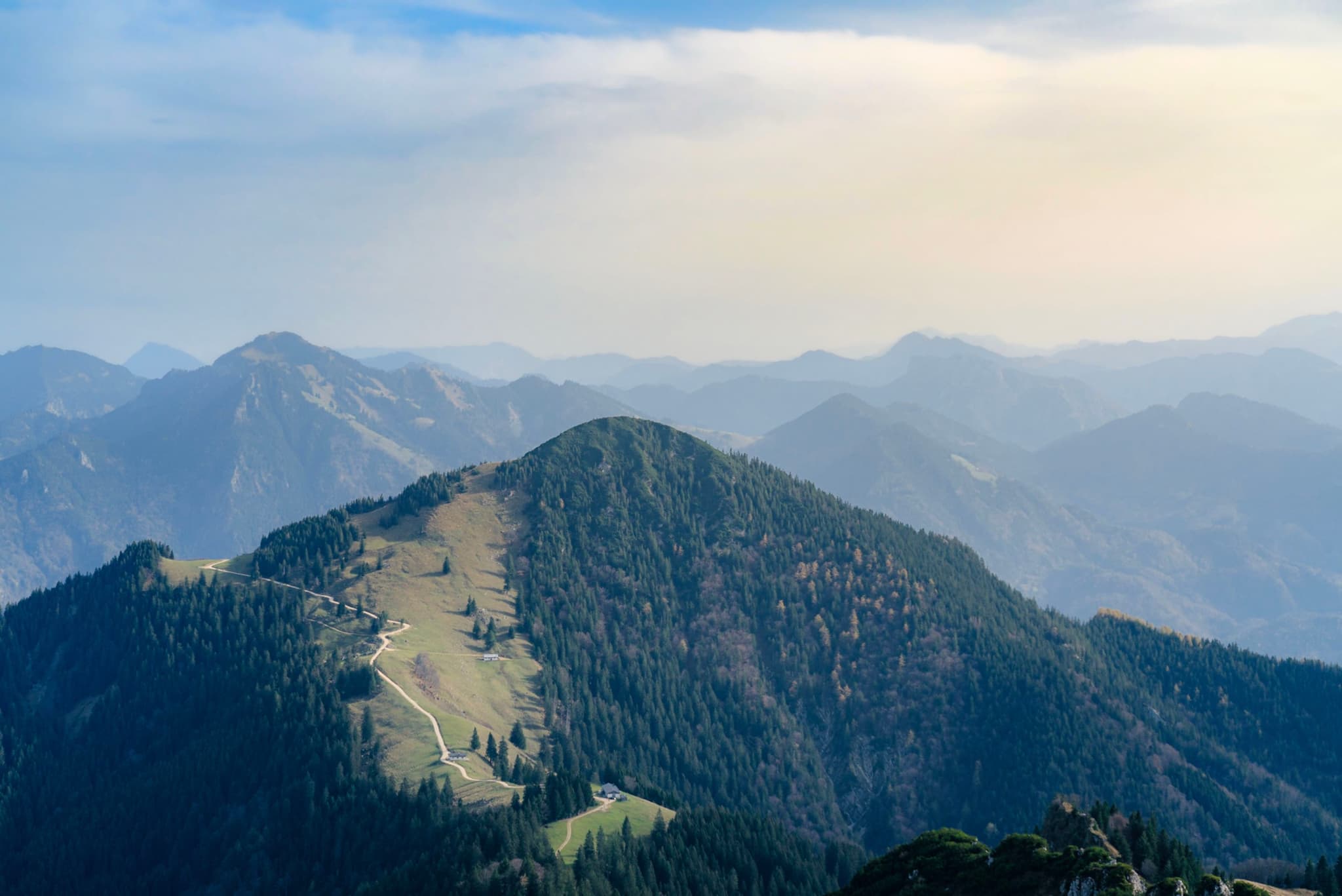 Sunlit central mountain summit with grassy slopes surrounded by hazy, receding blue ridgelines under a soft sky