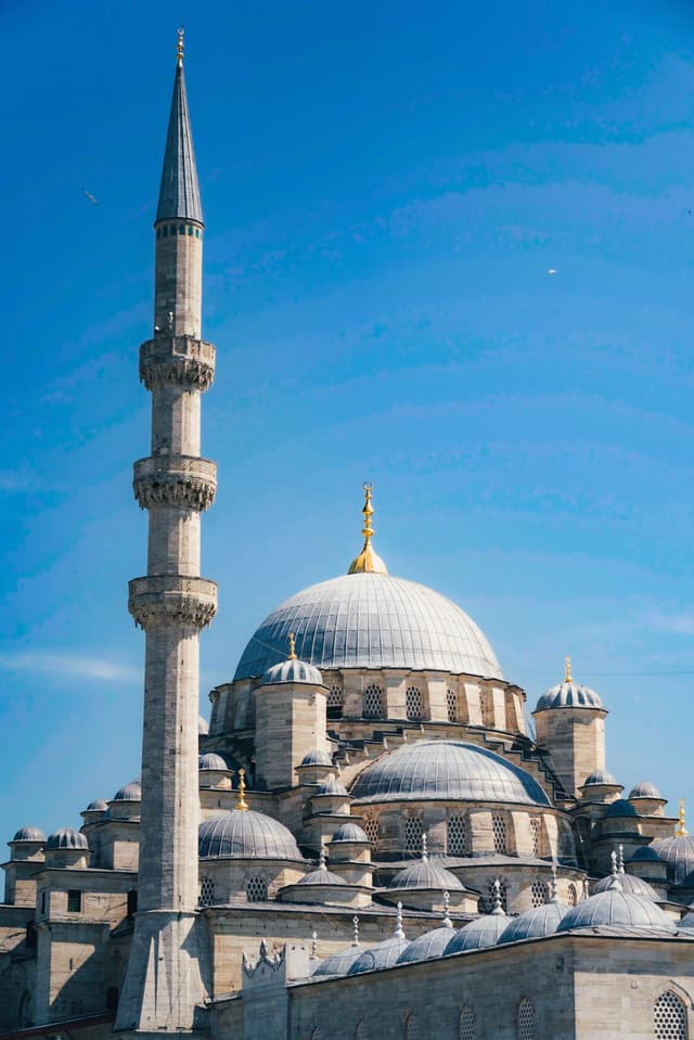 A grand mosque with a large central dome, multiple smaller domes, and a tall minaret against a clear blue sky