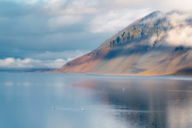 A serene mountain landscape with a calm lake in the foreground, partially shrouded in mist and clouds