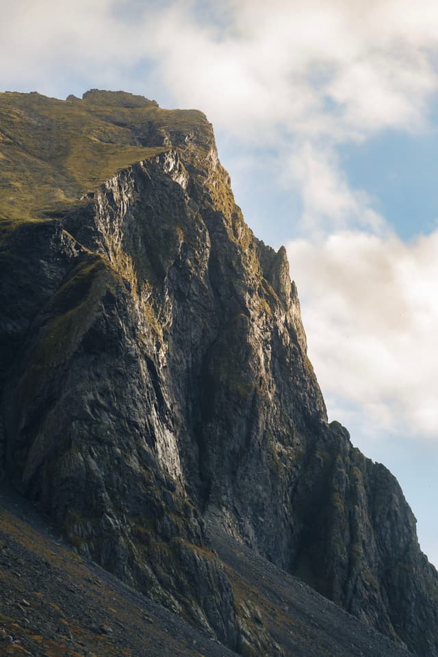 A rugged mountain peak with steep, rocky cliffs under a partly cloudy sky