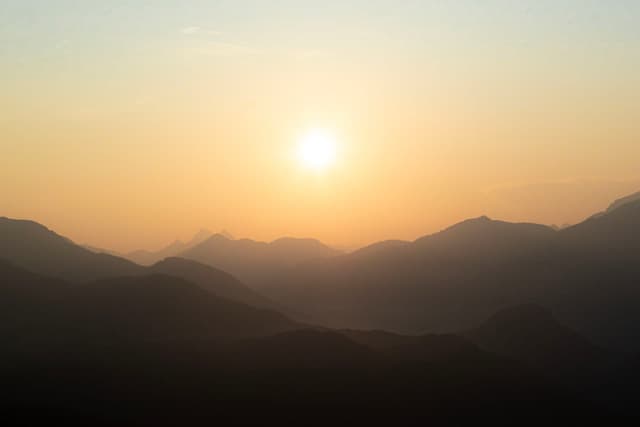 A serene landscape with a hazy sunset over rolling hills and mountains