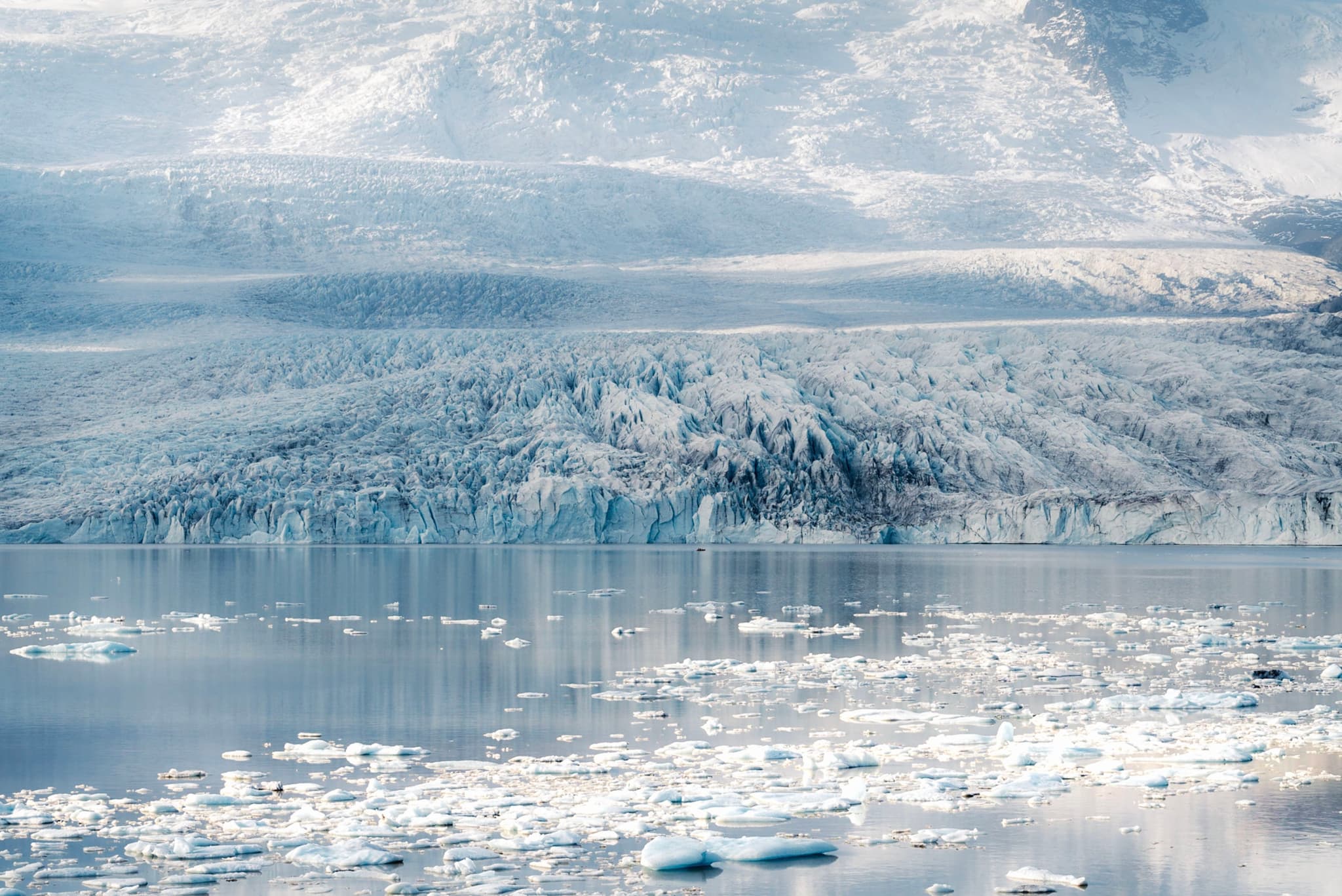 Serene icy fjord with scattered icebergs reflecting snow-covered mountains in pale winter light