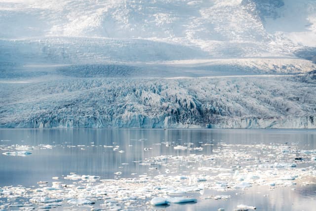 Serene icy fjord with scattered icebergs reflecting snow-covered mountains in pale winter light