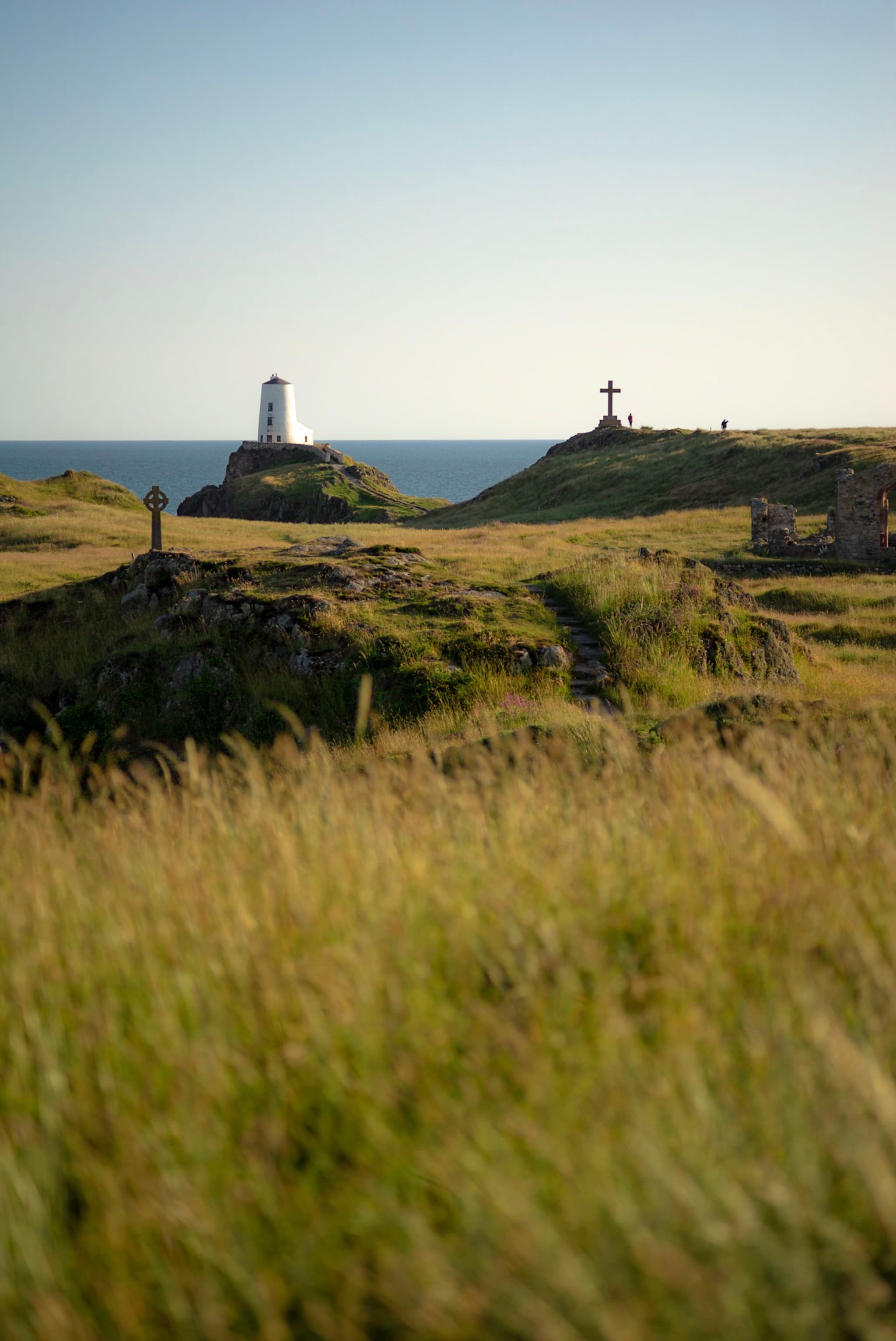 White lighthouse and stone cross standing on grassy coastal hills overlooking the sea