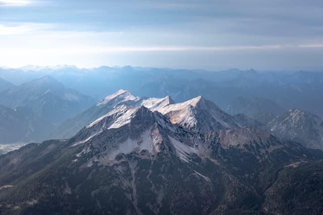 Snow-capped mountain peaks under a cloudy sky, with layers of distant mountains fading into the horizon