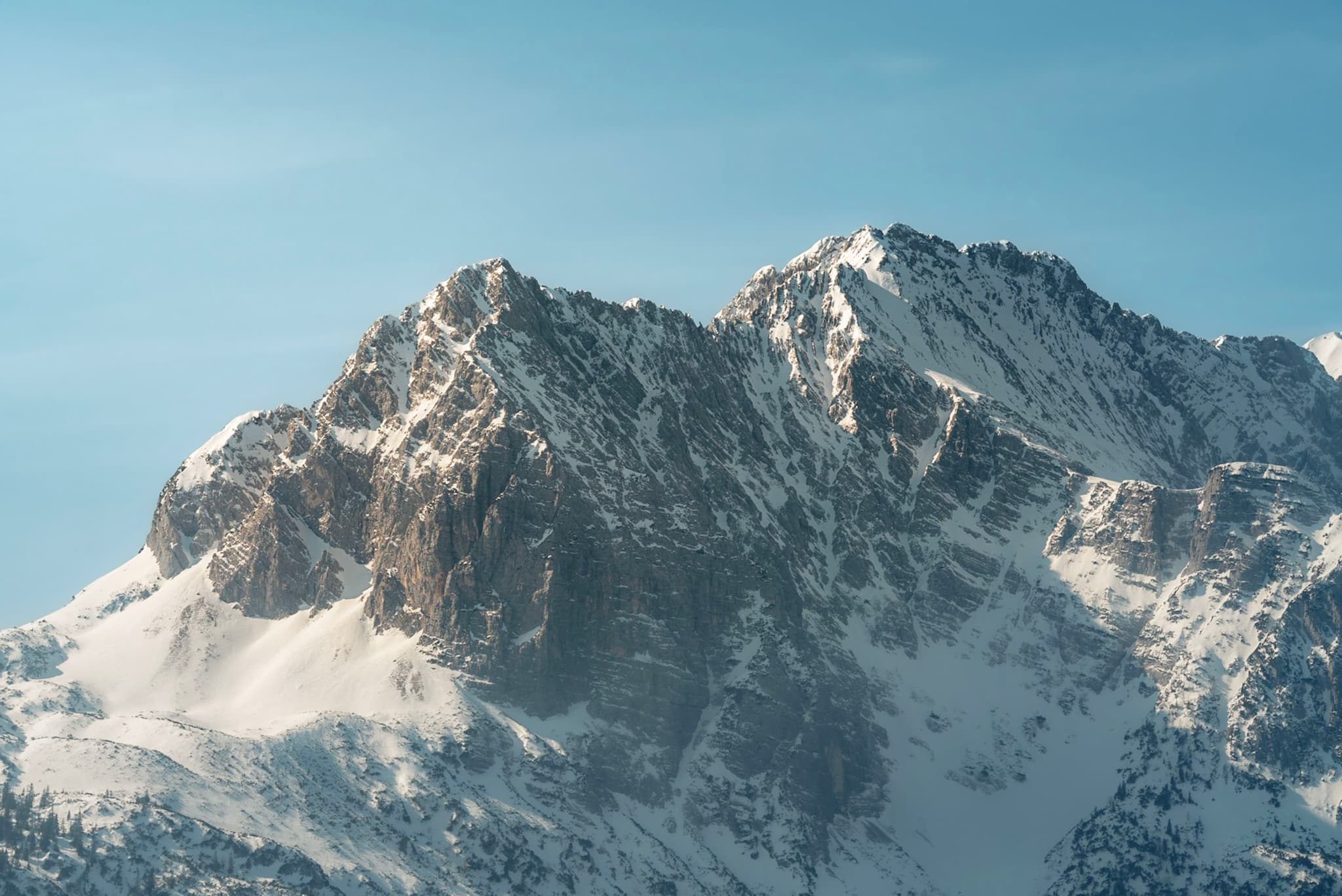 Sunlit snow-covered mountain peaks rising sharply against a clear blue sky