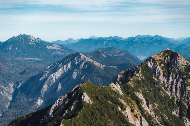 Jagged green and rocky mountain ridges receding into hazy blue distant ranges under a lightly clouded sky
