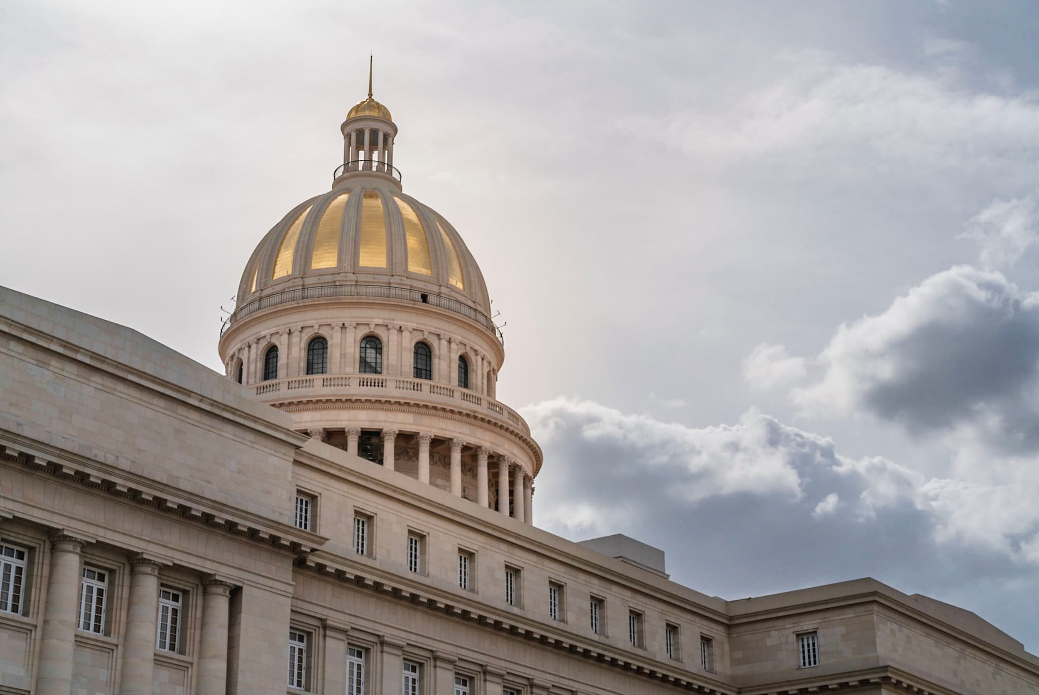 Majestic stone government building with a prominent golden dome under a cloudy sky