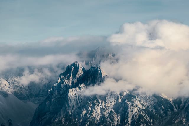 Snow-capped mountains partially covered by clouds under a blue sky