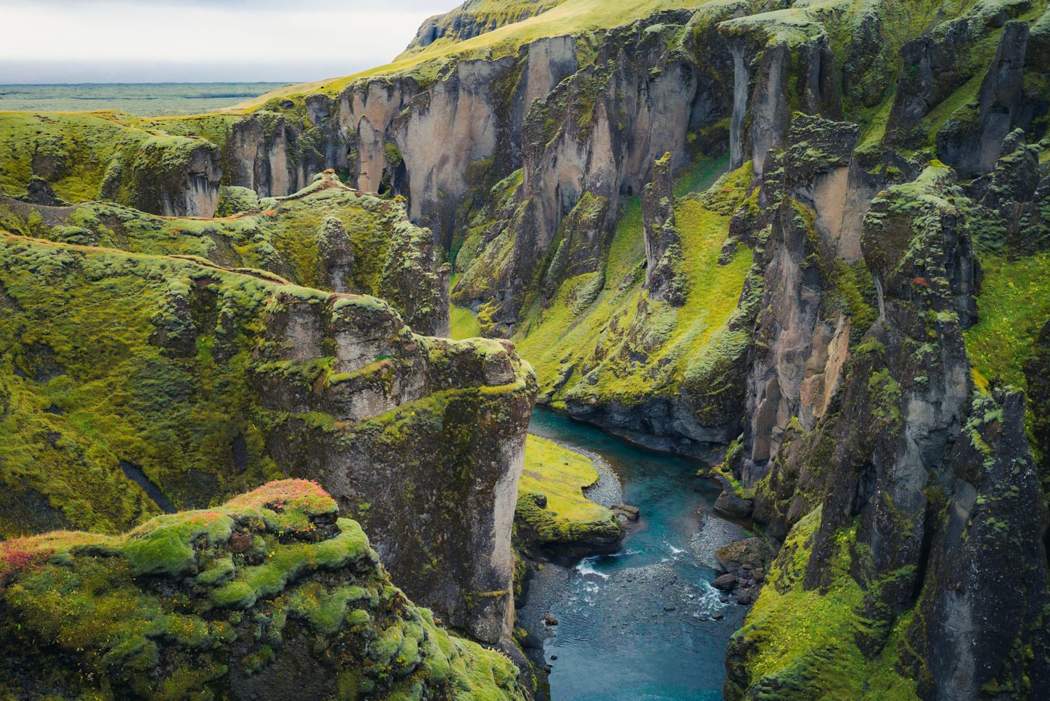 Deep river gorge winding between steep moss-covered cliffs in a lush, rugged landscape