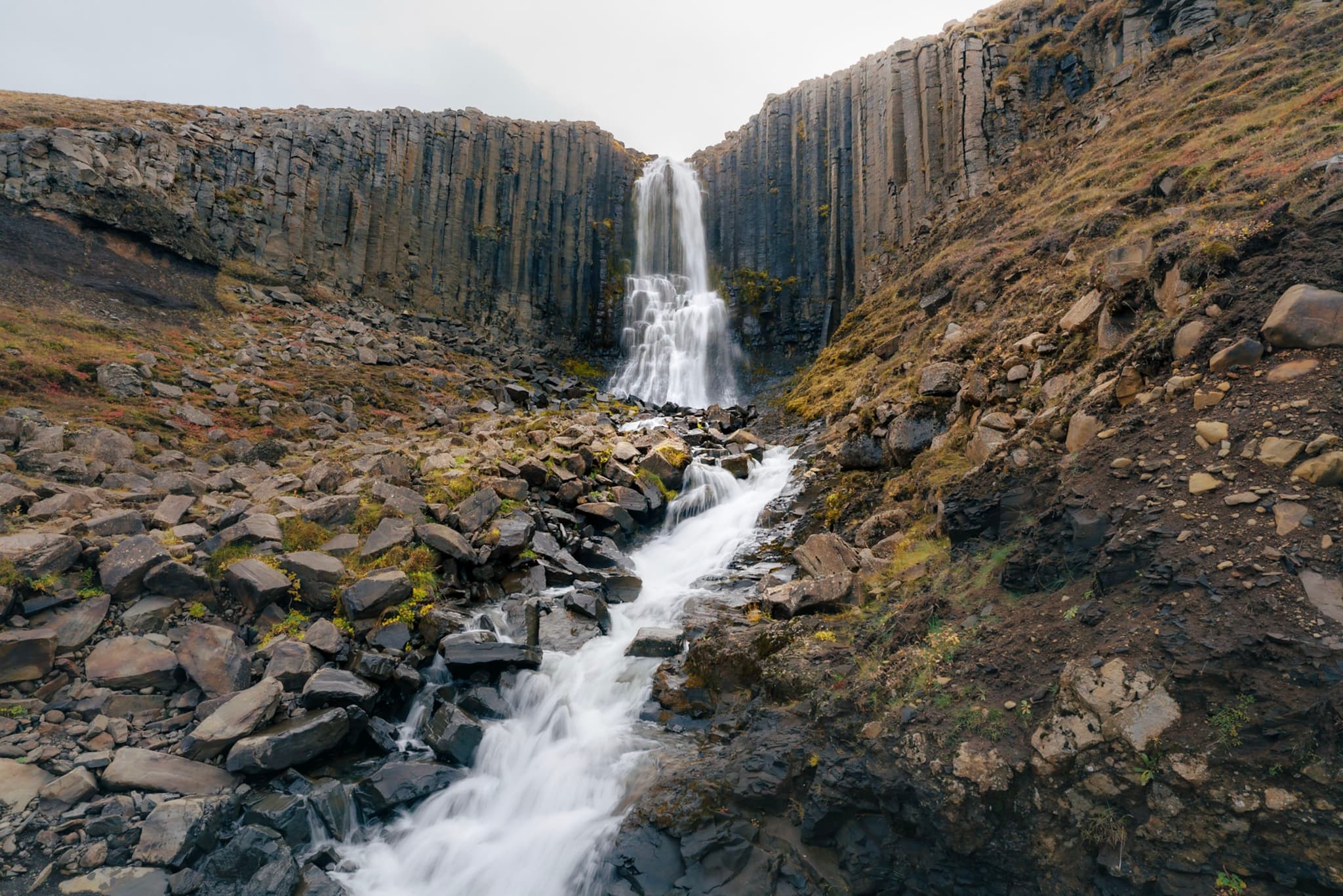 Tall waterfall cascading over basalt columns into a rocky stream valley