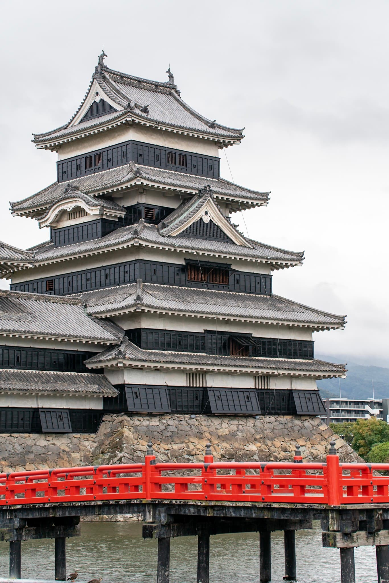 traditional Japanese castle rising above stone foundations with a vivid red wooden bridge crossing the surrounding moat