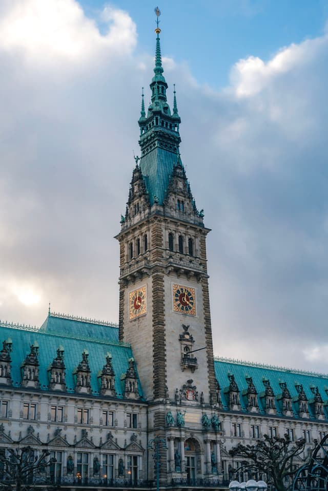 Tall historic clocktower with ornate architecture and green roof under a cloudy sky
