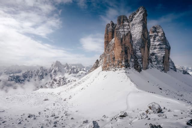 A snow-covered mountain landscape with towering rock formations under a partly cloudy sky