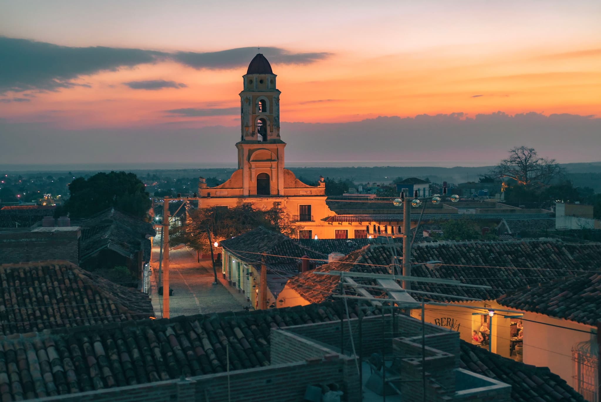 Old town rooftops leading toward an illuminated bell tower at sunset