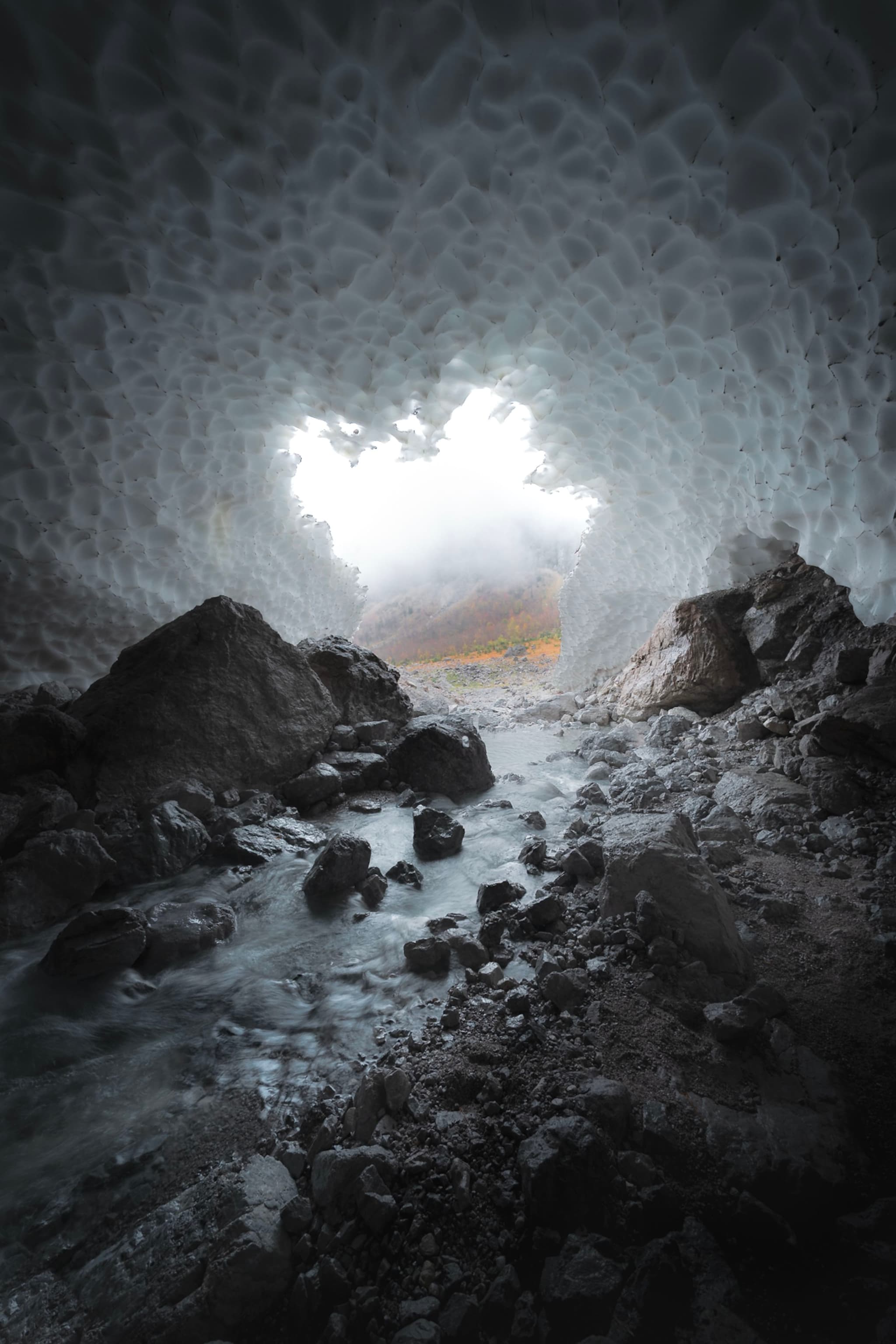 Rocky stream flowing through a dim ice cave toward a bright opening outside