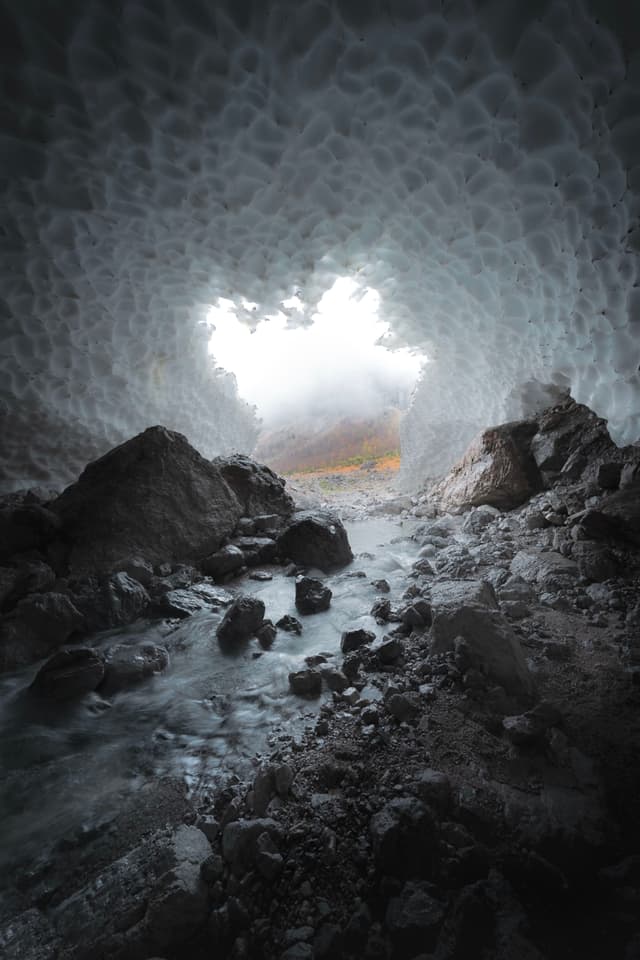 Rocky stream flowing through a dim ice cave toward a bright opening outside