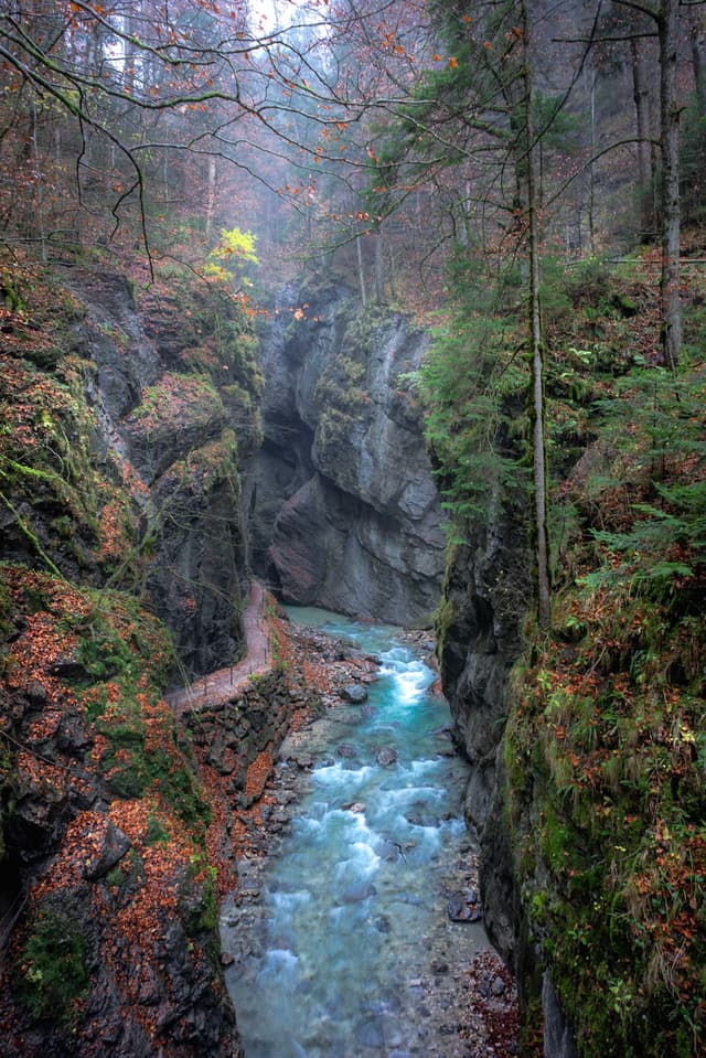 Narrow turquoise river flowing through a steep rocky canyon surrounded by autumn forest and misty light