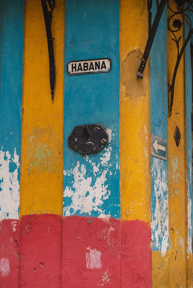 Colorful weathered wall in Habana with peeling paint in bold stripes of blue, yellow, and red and a street sign reading Habana