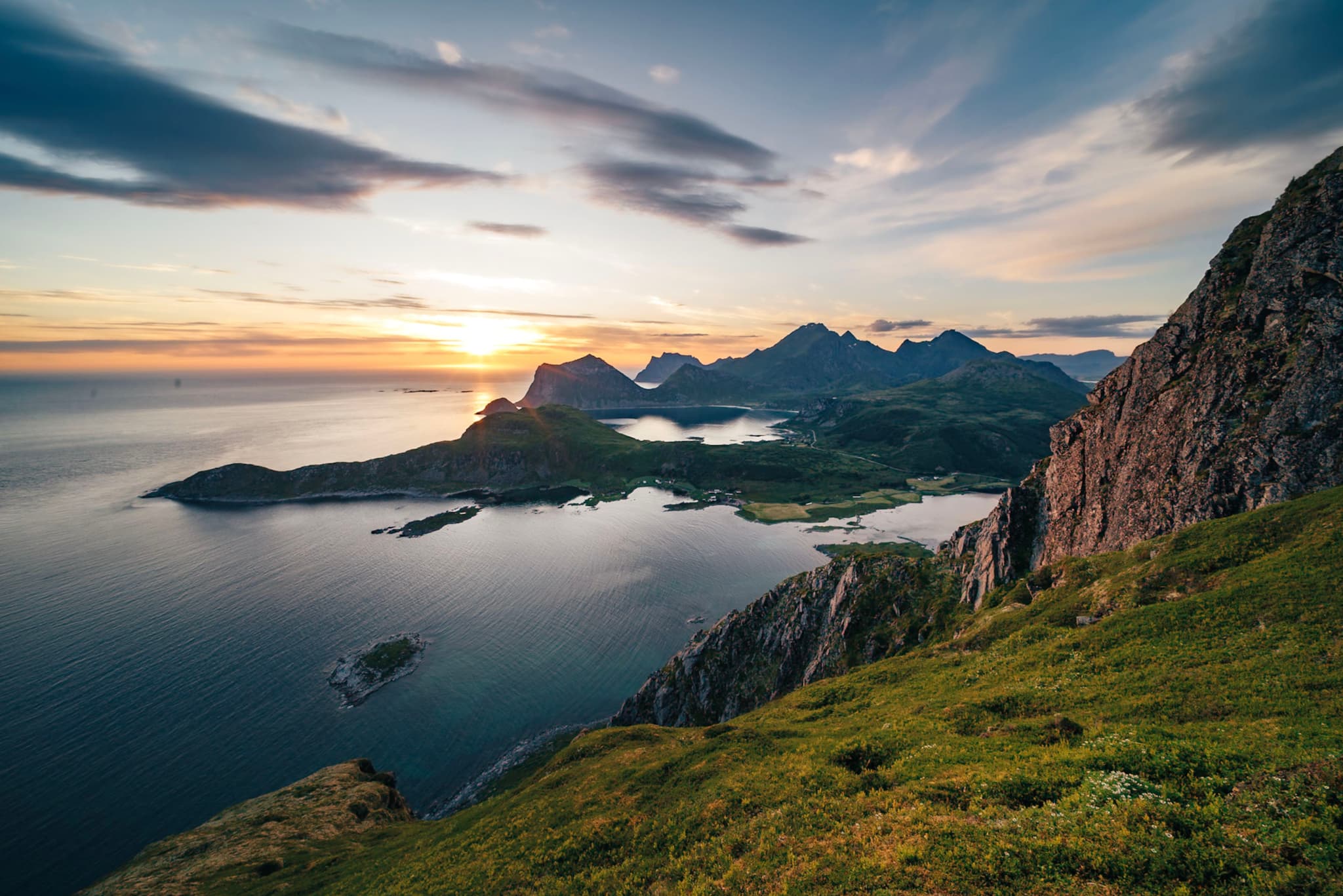 A scenic coastal landscape with mountains, a calm sea, and a sunset casting warm light over the horizon