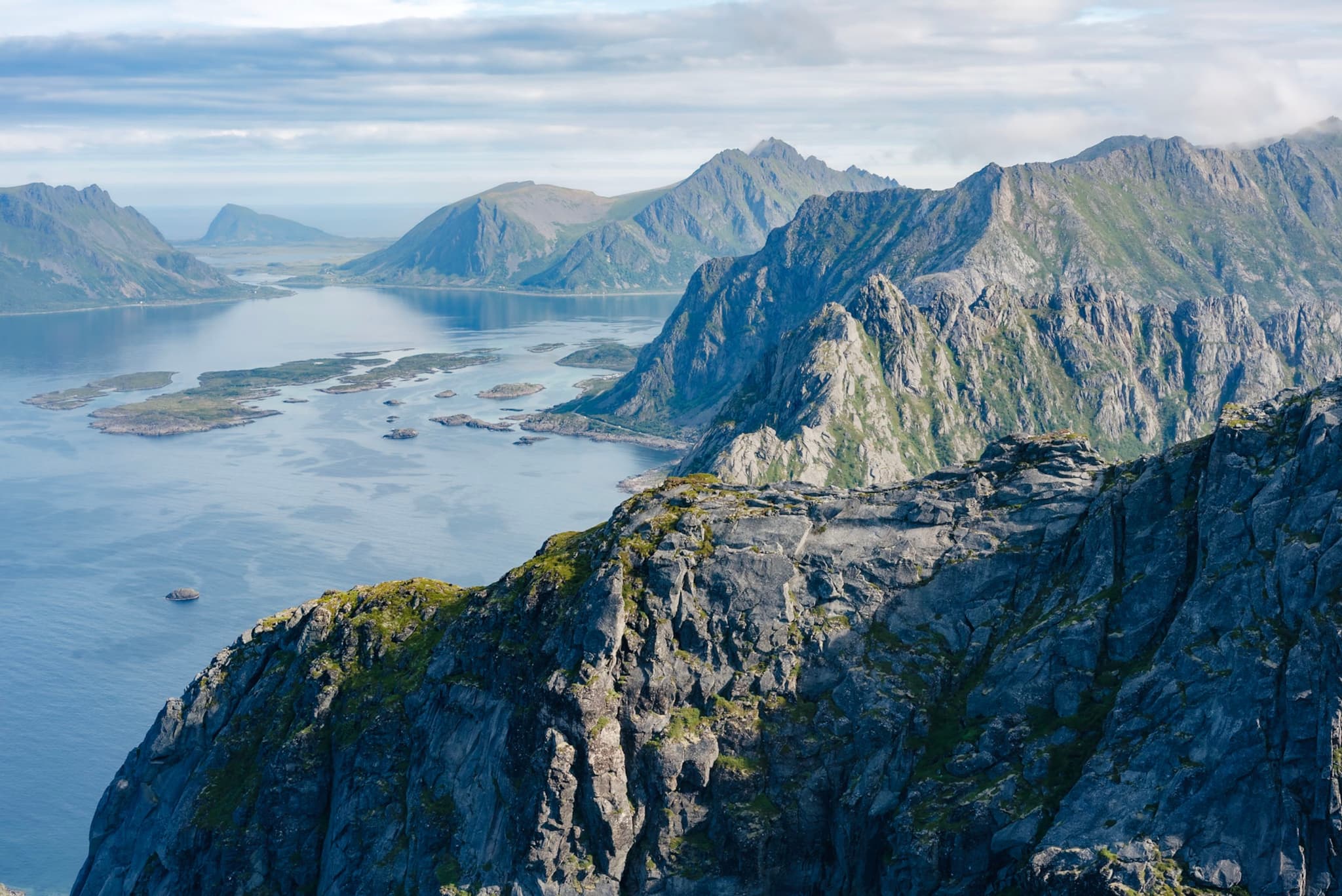 A scenic view of rugged mountains and a calm body of water, with scattered islands under a partly cloudy sky