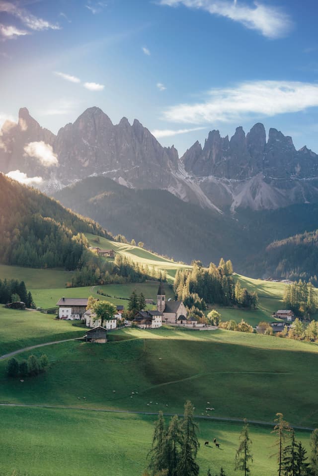 A picturesque alpine village nestled in a lush green valley, surrounded by towering, jagged mountains under a clear blue sky