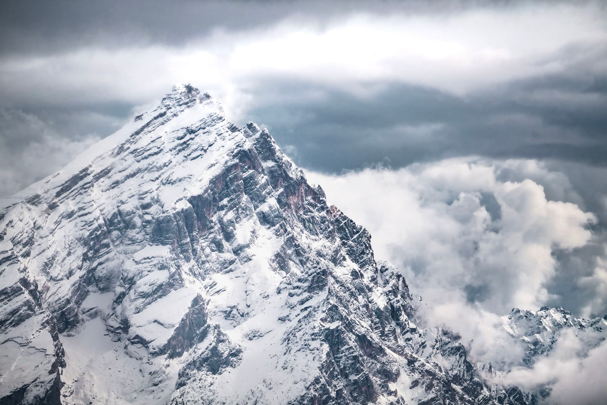 Jagged snow-covered mountain peak rising into thick storm clouds