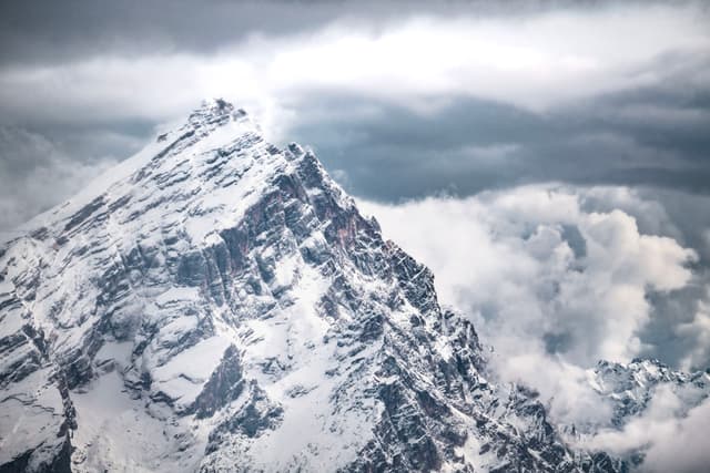 Jagged snow-covered mountain peak rising into thick storm clouds