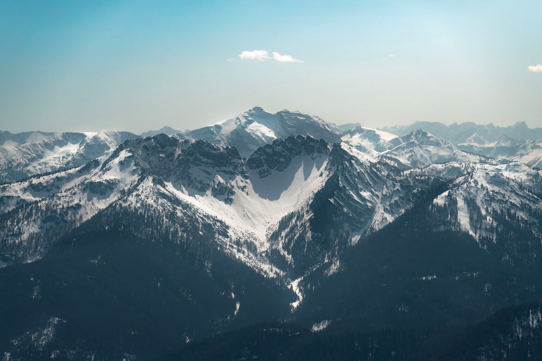 Snow-covered mountain range under a clear blue sky with a central valley and distant peaks