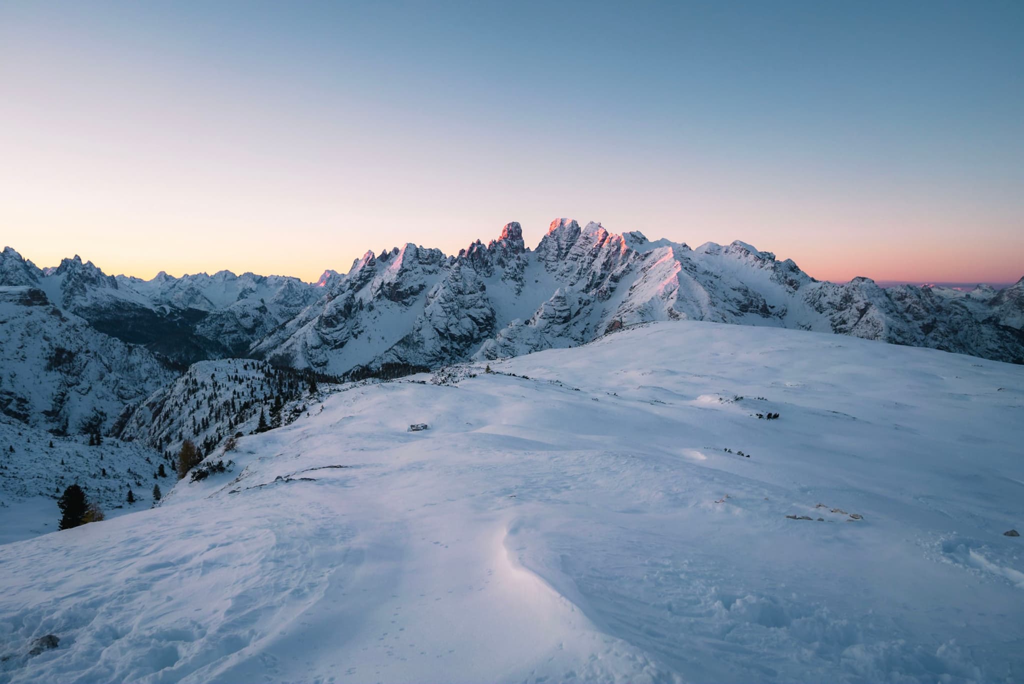 snow-covered mountain ridge at sunrise with pastel sky and distant jagged peaks
