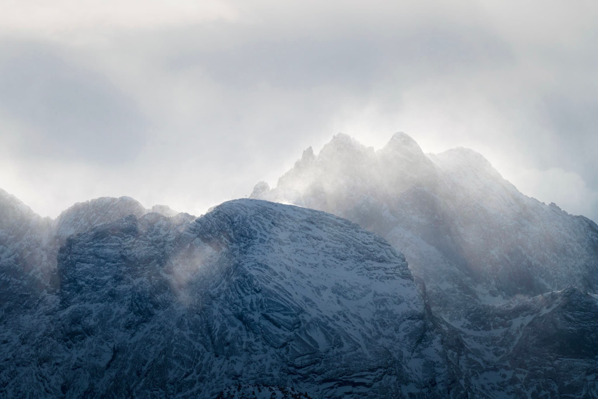Snow-dusted mountain peaks emerging through swirling mist and soft backlight