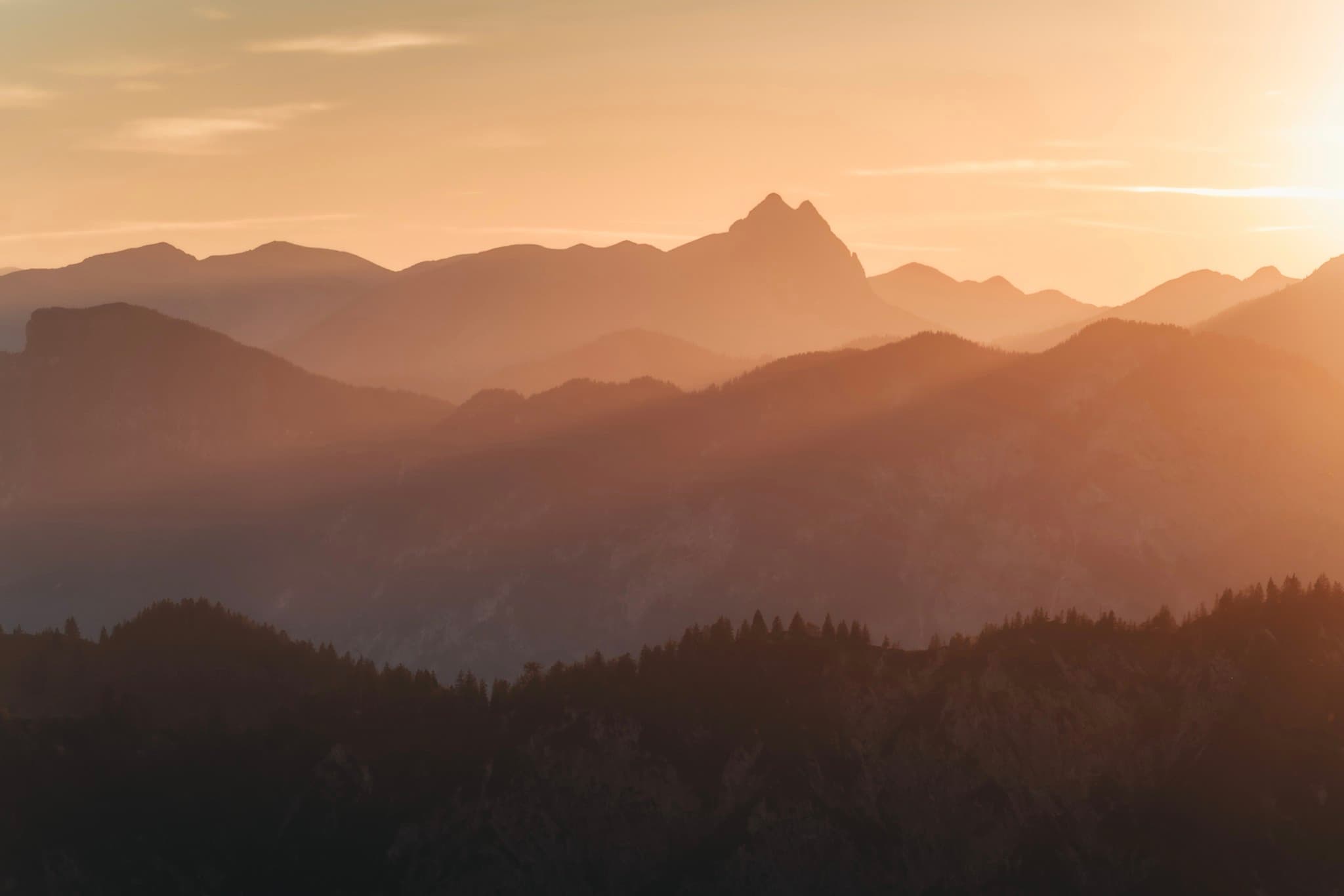 Layered mountain ridges glowing in warm sunset light with a hazy, golden sky