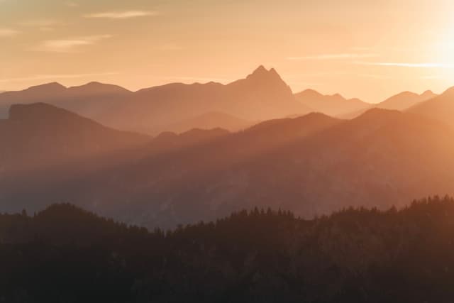 Layered mountain ridges glowing in warm sunset light with a hazy, golden sky