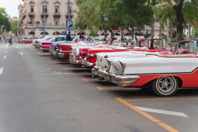 Row of colorful vintage convertibles parked along a city street with historic buildings and trees in the background
