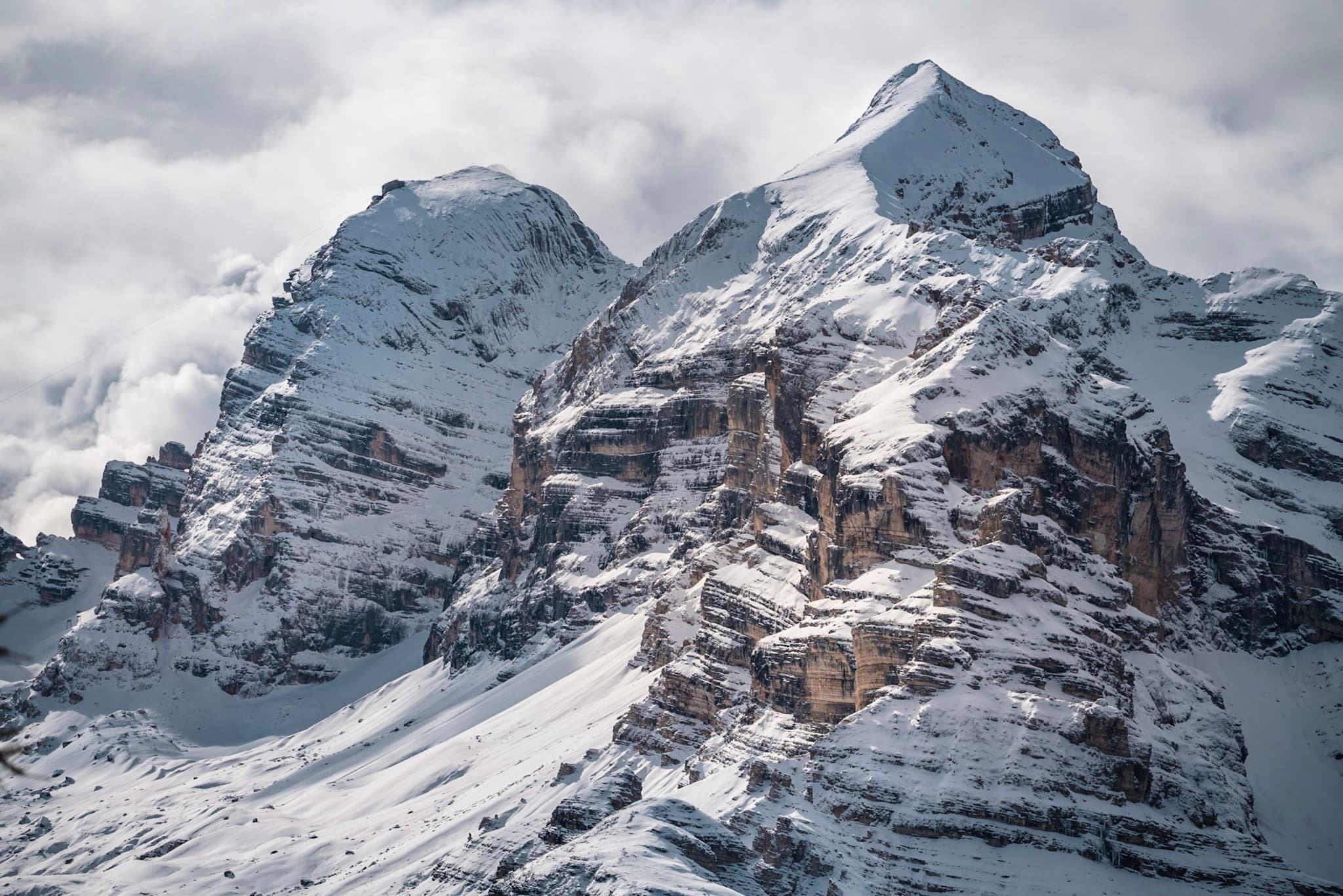 Snow-covered twin mountain peaks with rugged rocky faces rising into a cloudy sky