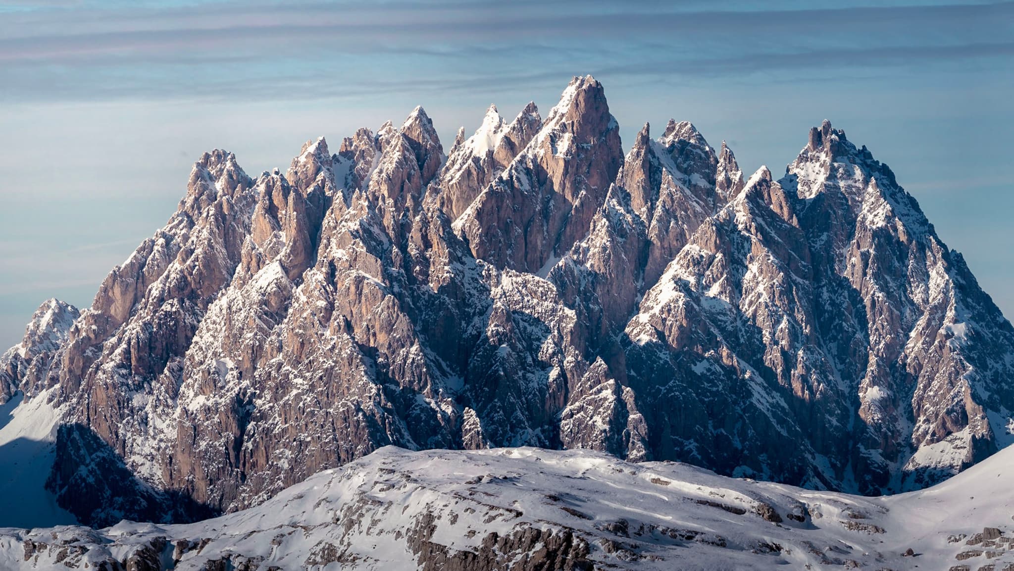 towering jagged mountain range covered in snow under a pale sky