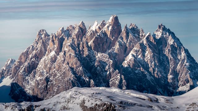 towering jagged mountain range covered in snow under a pale sky