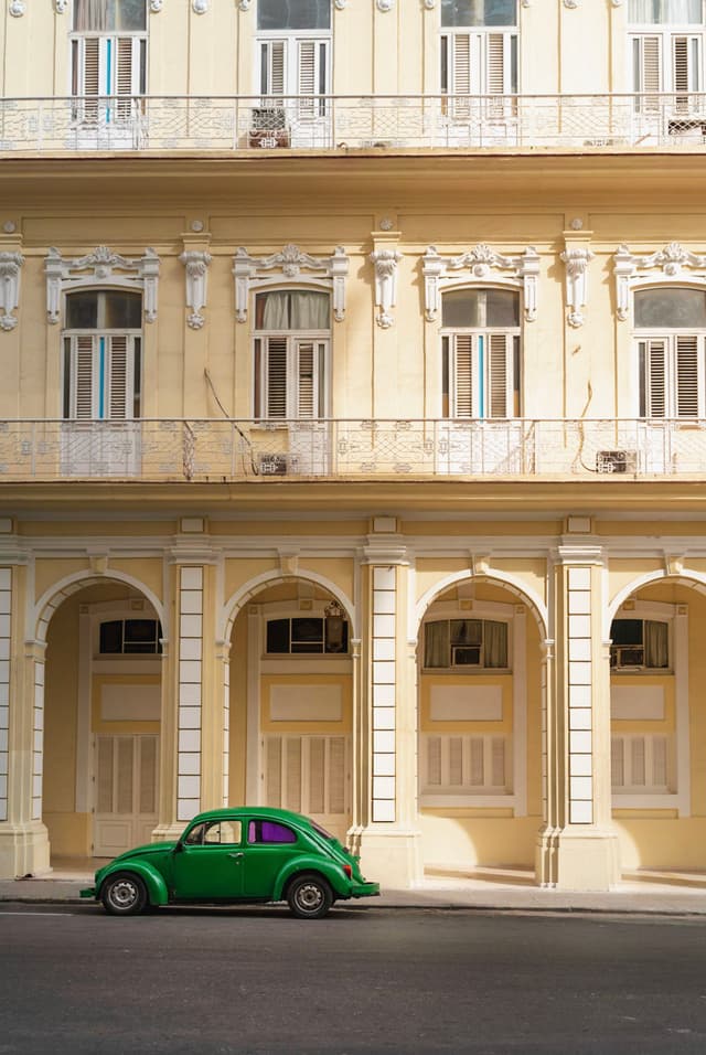 Bright green vintage car parked along the arches of a pale yellow classical building facade