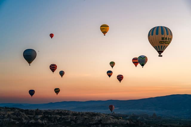 Hot air balloons floating over a landscape at sunrise or sunset, with a colorful sky and distant hills