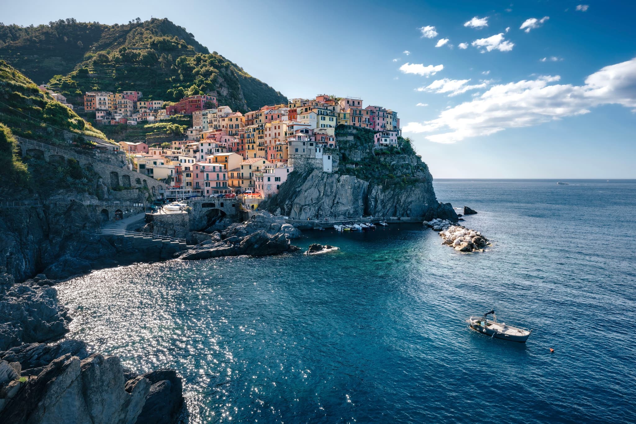 A coastal village with colorful buildings perched on a cliffside, overlooking a calm blue sea with a small boat nearby