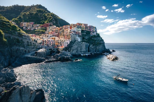 A coastal village with colorful buildings perched on a cliffside, overlooking a calm blue sea with a small boat nearby