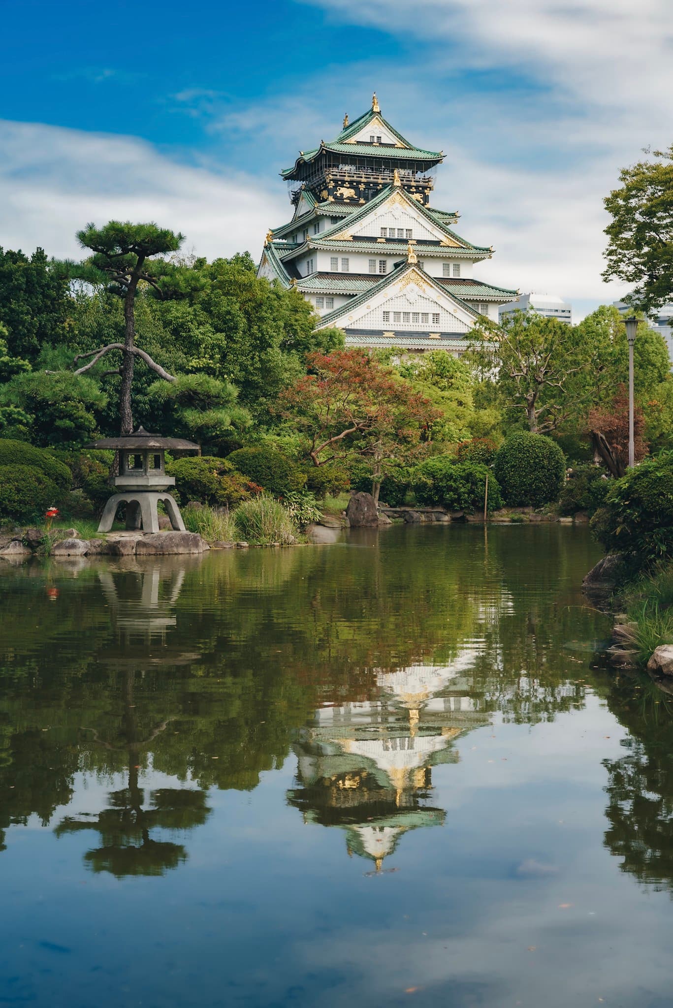 Japanese castle surrounded by lush gardens reflected in a still pond under a blue sky