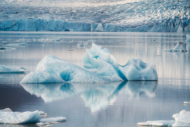 Floating iceberg reflected in calm glacial lagoon surrounded by icy mountains