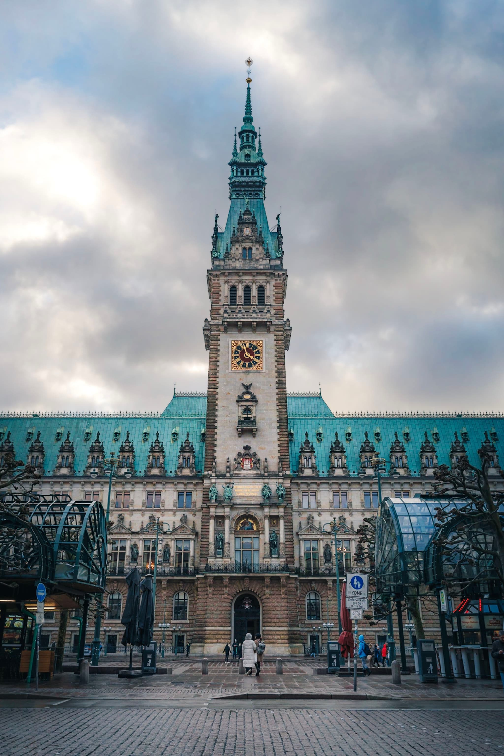 ornate historic tower with central clock rising above a public courtyard under a cloudy sky
