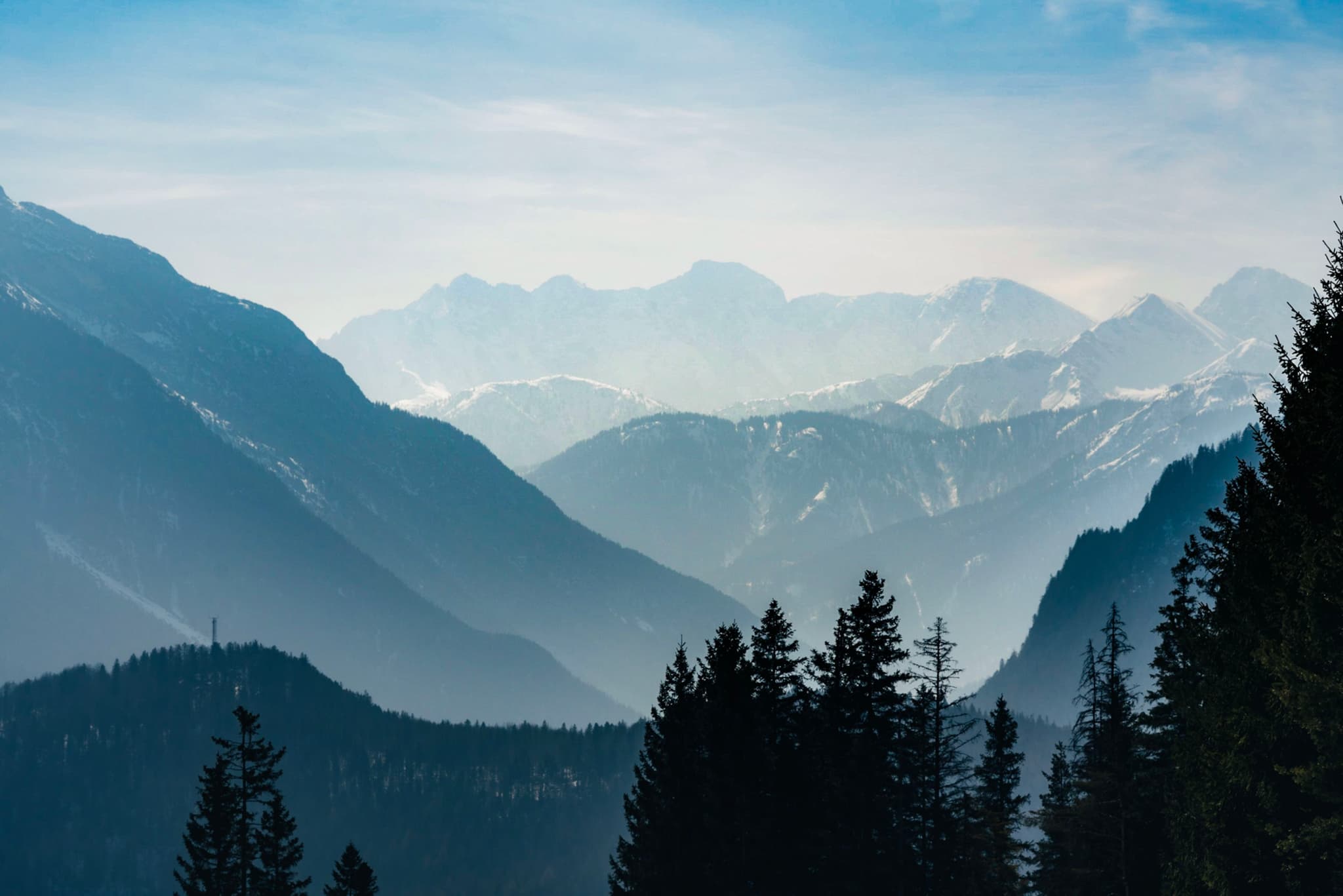 A serene mountain landscape with layers of misty blue peaks and silhouetted pine trees in the foreground