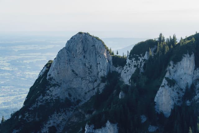 A rugged mountain peak with patches of greenery and a distant view of the landscape below