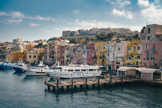 Colorful waterfront town with boats docked along a wooden pier beneath a partly cloudy sky