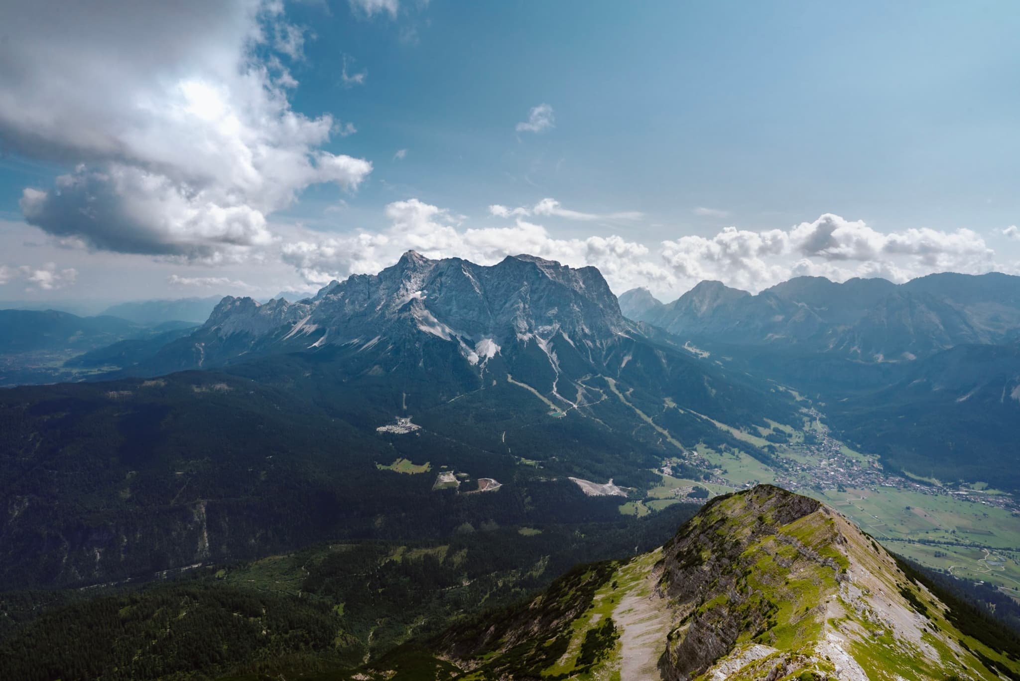 High vantage over a rugged mountain range with a green valley below under a bright, partly cloudy sky