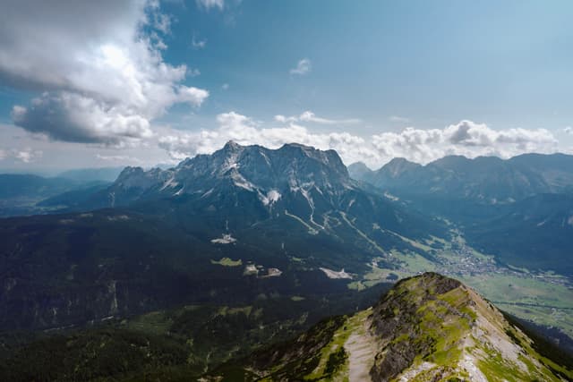 High vantage over a rugged mountain range with a green valley below under a bright, partly cloudy sky