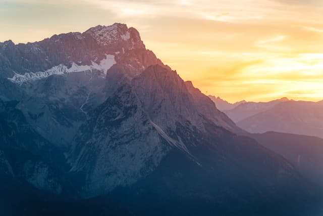 A majestic mountain range at sunset, with a glowing sky and rugged peaks